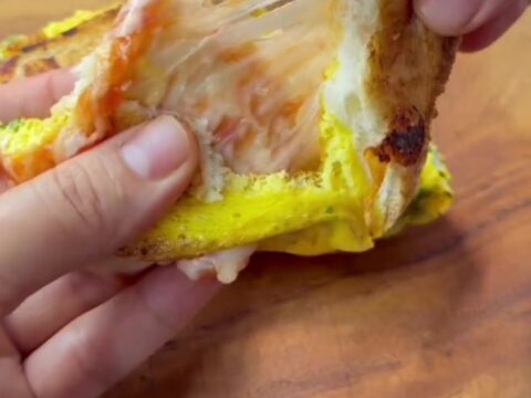Golden brown egg toast sandwich sliced in half with melted cheese pulling apart