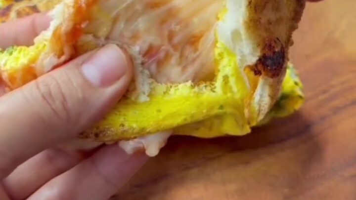 Golden brown egg toast sandwich sliced in half with melted cheese pulling apart