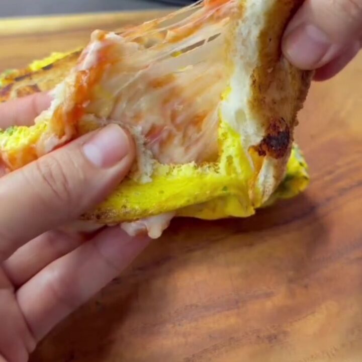 Golden brown egg toast sandwich sliced in half with melted cheese pulling apart