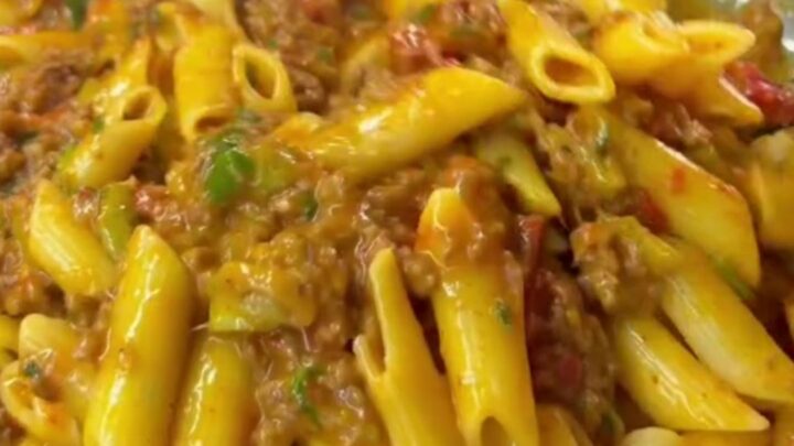 Steaming penne pasta with meatballs and vegetables in a rich tomato sauce, garnished with parsley and Parmesan.