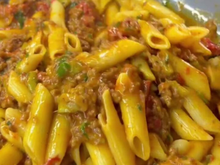 Steaming penne pasta with meatballs and vegetables in a rich tomato sauce, garnished with parsley and Parmesan.