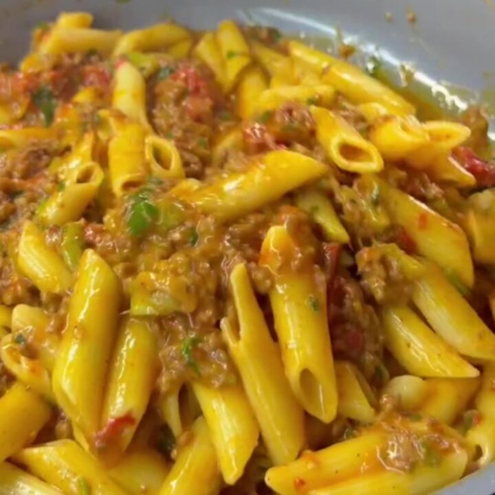 Steaming penne pasta with meatballs and vegetables in a rich tomato sauce, garnished with parsley and Parmesan.
