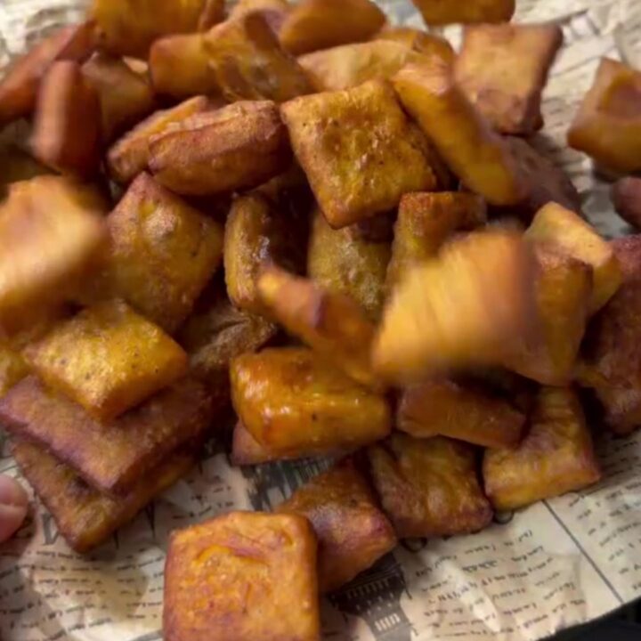 A pile of golden crispy potato snack chips on a paper towel, with one chip snapped in half showing airy interior.