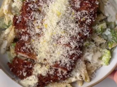 Crispy chicken Caesar pasta salad in a bowl, topped with golden chicken strips and shaved Parmesan