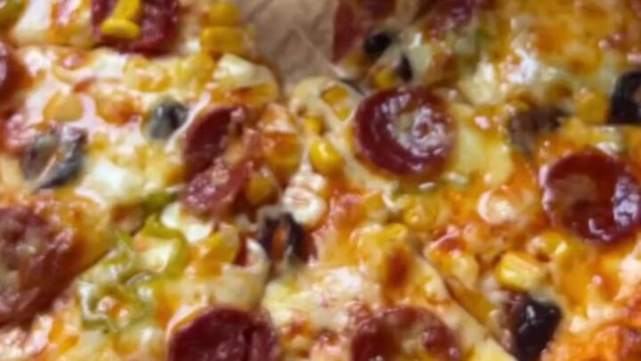 Bakery-style homemade pizza with stretchy cheese pull on a parchment-lined baking sheet
