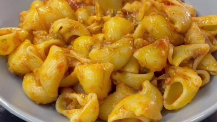 Spoon lifting cheesy pipe rigate pasta with long molten cheese strings and vegetable bits