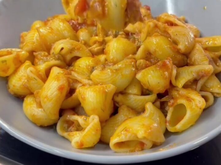 Spoon lifting cheesy pipe rigate pasta with long molten cheese strings and vegetable bits