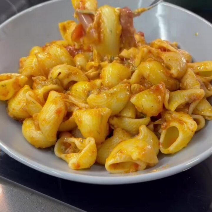 Spoon lifting cheesy pipe rigate pasta with long molten cheese strings and vegetable bits