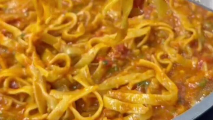 Twirled tagliatelle with creamy vegetable sauce on a white plate, garnished with Parmesan