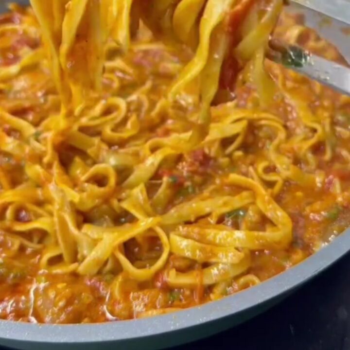 Twirled tagliatelle with creamy vegetable sauce on a white plate, garnished with Parmesan