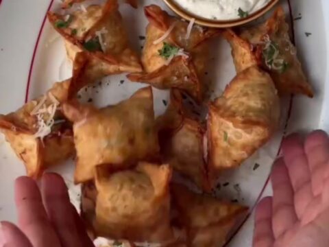 Crispy golden chicken rangoons with a creamy garlic Parmesan dip, one broken open showing the filling