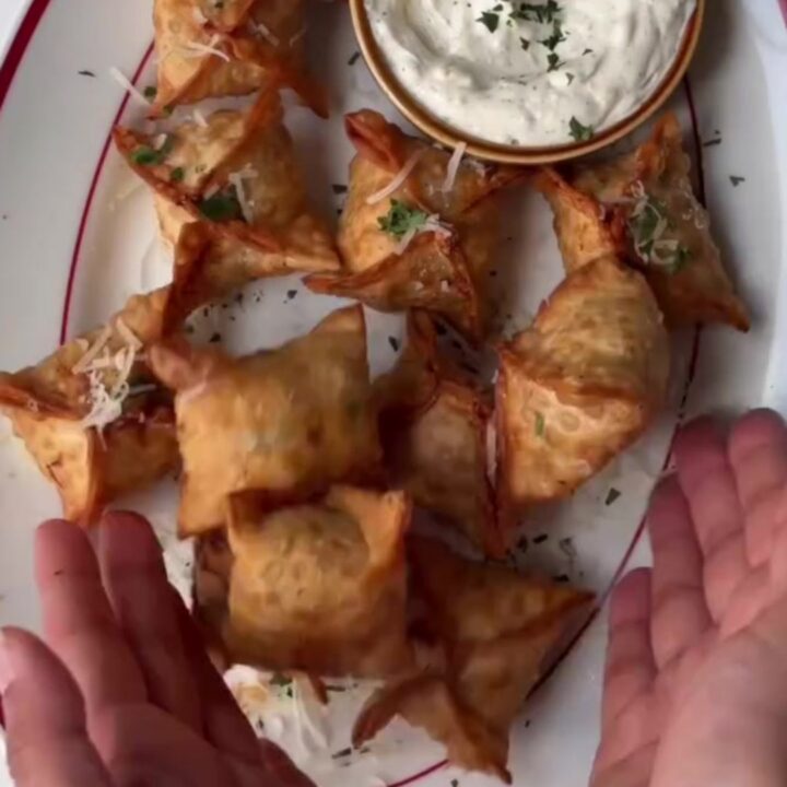 Crispy golden chicken rangoons with a creamy garlic Parmesan dip, one broken open showing the filling