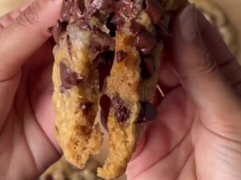 Warm chocolate chip cookie pulled apart with melted dark chocolate stretching between halves