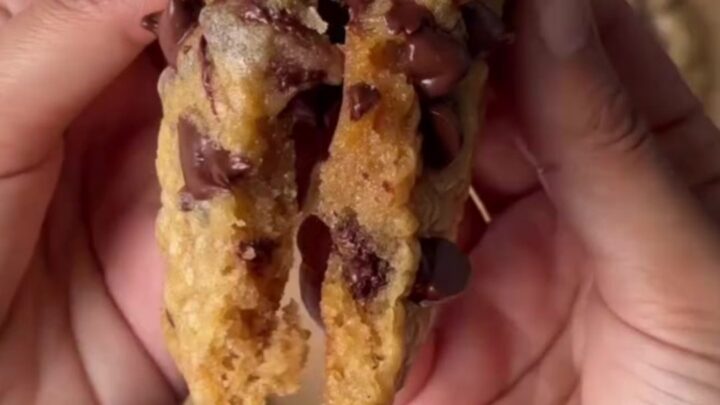 Warm chocolate chip cookie pulled apart with melted dark chocolate stretching between halves