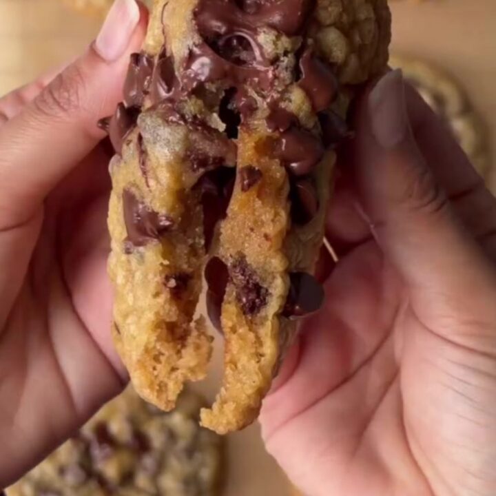 Warm chocolate chip cookie pulled apart with melted dark chocolate stretching between halves