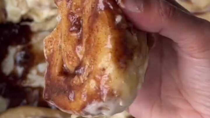 Warm cinnamon rolls with cream cheese frosting melting into the swirls, pulled apart in a baking dish