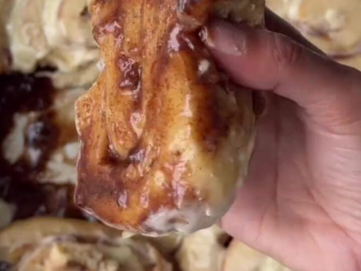 Warm cinnamon rolls with cream cheese frosting melting into the swirls, pulled apart in a baking dish