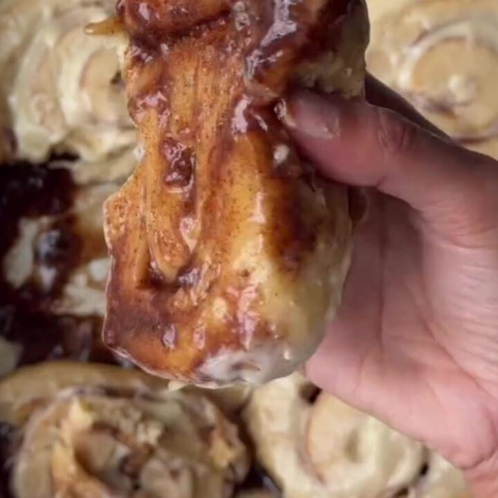 Warm cinnamon rolls with cream cheese frosting melting into the swirls, pulled apart in a baking dish