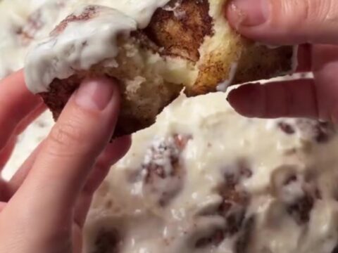 Warm cinnamon pull-apart rolls with cream cheese glaze, one roll being pulled apart showing stringy caramel.