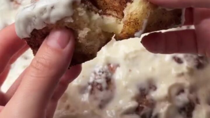 Warm cinnamon pull-apart rolls with cream cheese glaze, one roll being pulled apart showing stringy caramel.