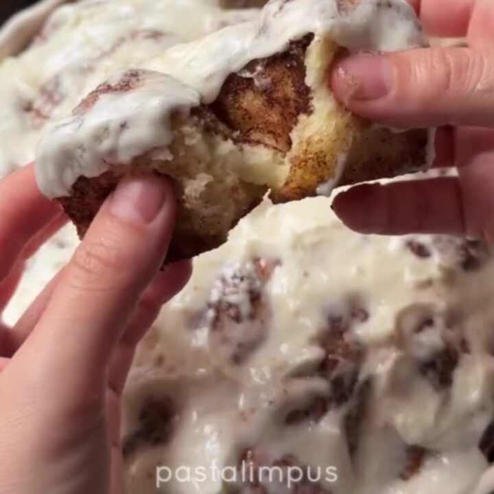 Warm cinnamon pull-apart rolls with cream cheese glaze, one roll being pulled apart showing stringy caramel.