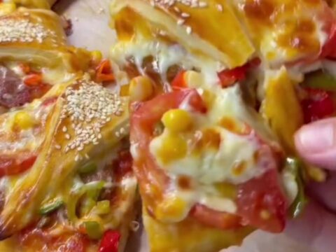 Golden crown pizza ring with bubbling mozzarella and sucuk, sesame-crusted, on parchment