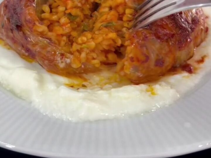 Baked cabbage dome sliced on a bed of garlic yogurt, showing spiced beef and rice filling