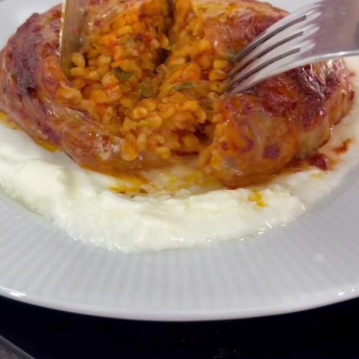 Baked cabbage dome sliced on a bed of garlic yogurt, showing spiced beef and rice filling
