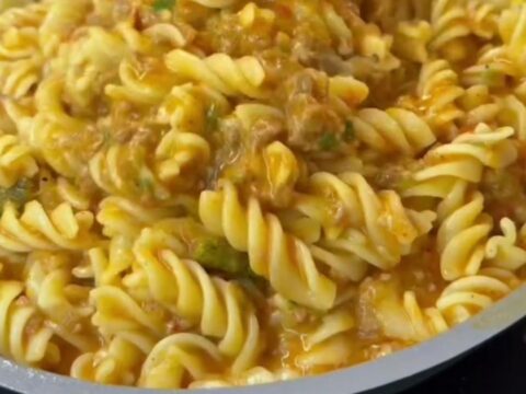 Spoon scooping steaming fusilli with meatball sauce onto a plate, garnished with parsley and cheese.