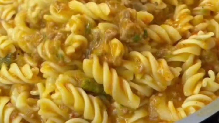 Spoon scooping steaming fusilli with meatball sauce onto a plate, garnished with parsley and cheese.
