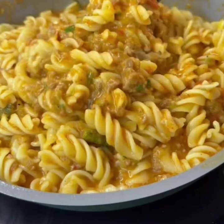 Spoon scooping steaming fusilli with meatball sauce onto a plate, garnished with parsley and cheese.