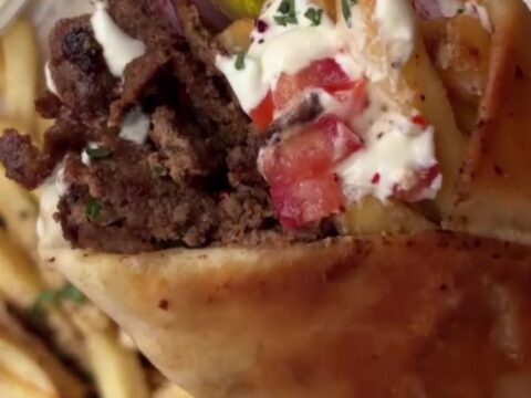 Crispy beef shawarma wrap sliced diagonally, showing beef ribbons, fries, and garlic sauce.