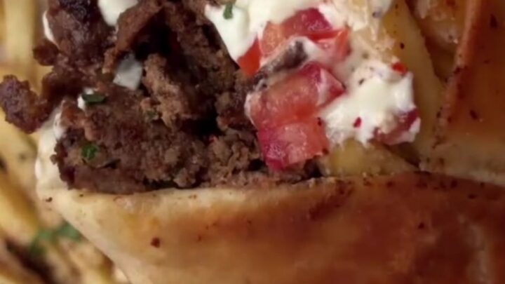 Crispy beef shawarma wrap sliced diagonally, showing beef ribbons, fries, and garlic sauce.