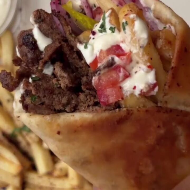 Crispy beef shawarma wrap sliced diagonally, showing beef ribbons, fries, and garlic sauce.