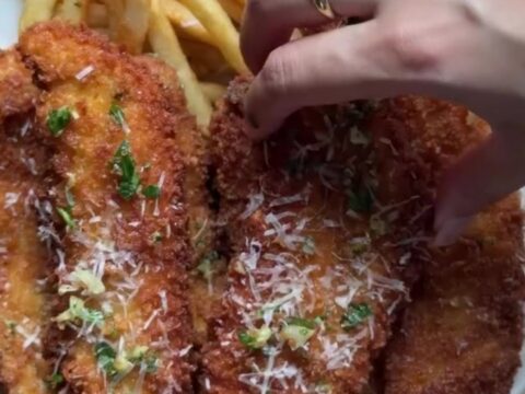 Crispy garlic Parmesan chicken tenders piled on a plate with a bowl of chili sauce for dipping.