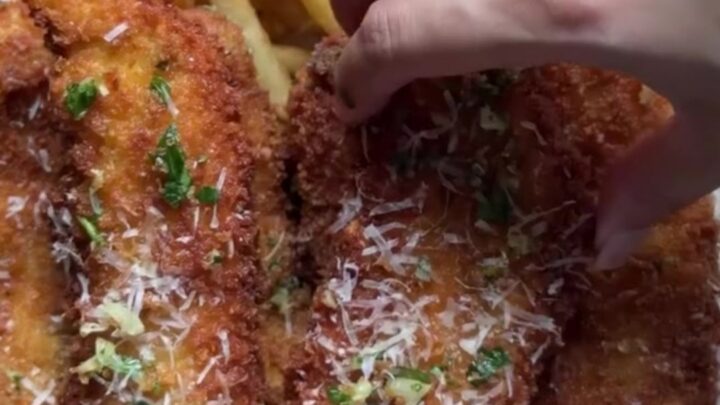 Crispy garlic Parmesan chicken tenders piled on a plate with a bowl of chili sauce for dipping.