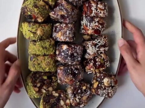 Sliced no-bake cardamom date nut rolls showing pistachio and walnut pieces in dark date caramel.