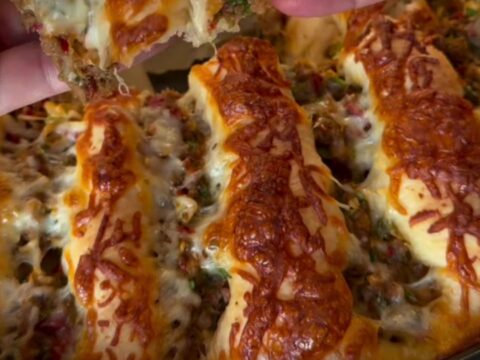 Golden pull-apart pide bread with seasoned ground beef and melted cheese, showing a slice being lifted with a spatula.
