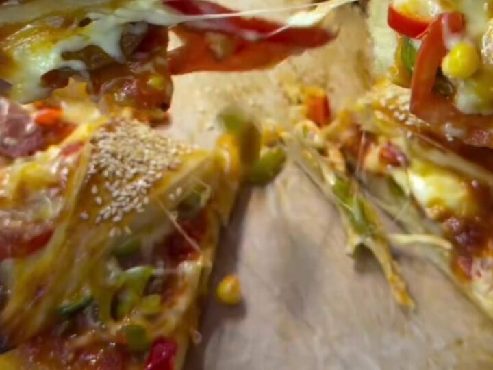 Golden crown pizza ring on parchment, with sesame seeds and melted cheese visible in the folds.
