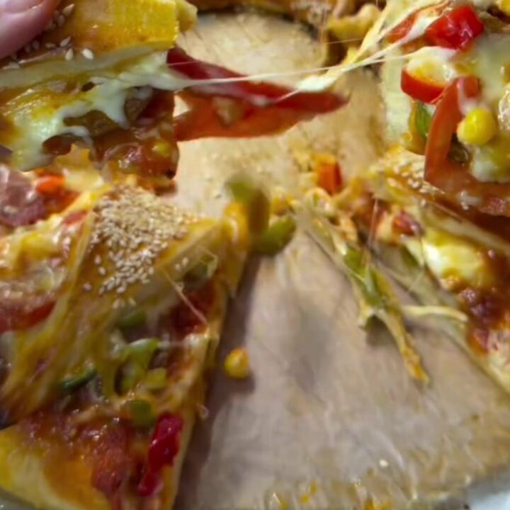 Golden crown pizza ring on parchment, with sesame seeds and melted cheese visible in the folds.