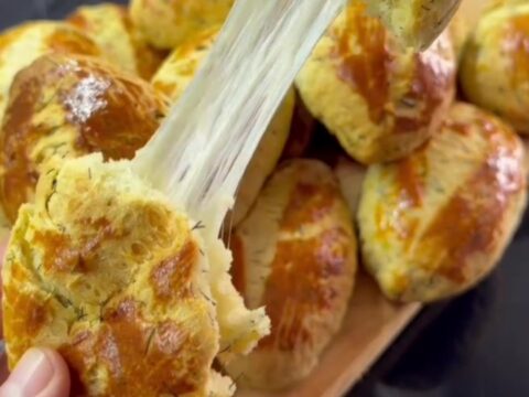 Golden pogaca buns with glossy tops and fork-scored pattern on a baking sheet.