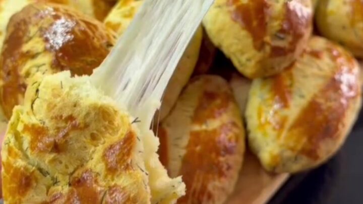 Golden pogaca buns with glossy tops and fork-scored pattern on a baking sheet.