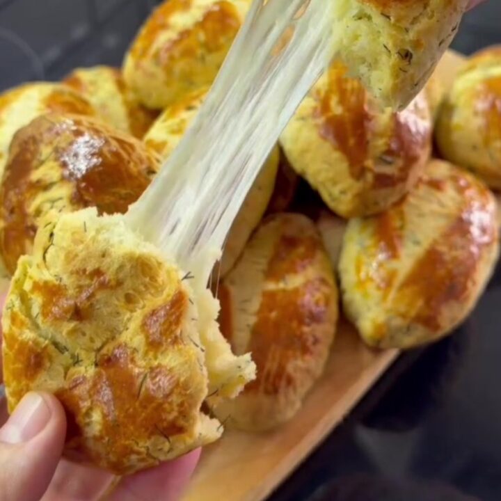 Golden pogaca buns with glossy tops and fork-scored pattern on a baking sheet.