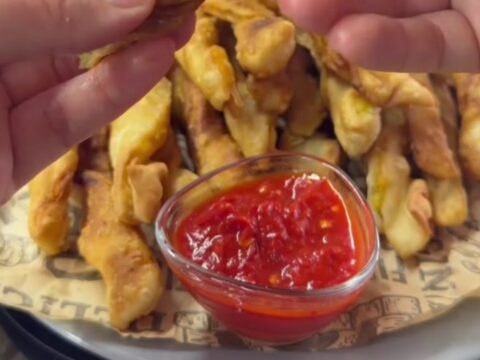 Twisted golden potato churro fries with sweet chili sauce, one fry dipped and showing a crispy shell and soft interior.