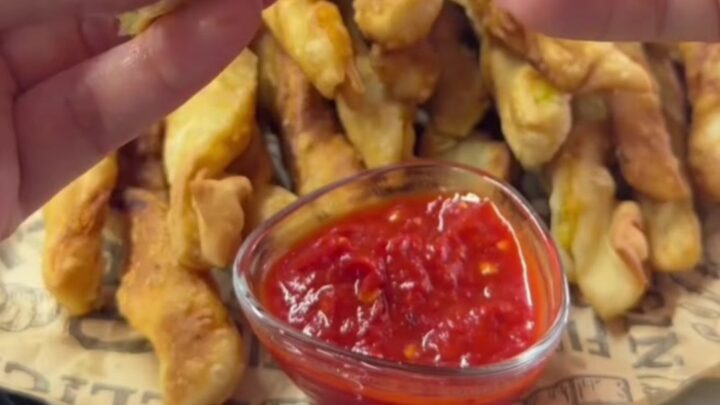 Twisted golden potato churro fries with sweet chili sauce, one fry dipped and showing a crispy shell and soft interior.