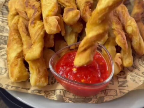 Golden spiral potato fries piled on a tray, one snapped in half showing a crisp, airy interior.