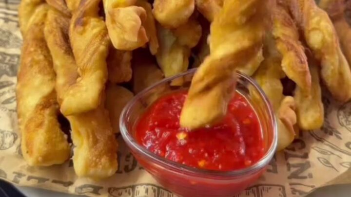 Golden spiral potato fries piled on a tray, one snapped in half showing a crisp, airy interior.