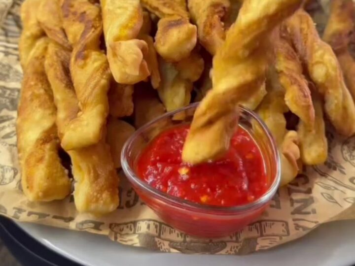 Golden spiral potato fries piled on a tray, one snapped in half showing a crisp, airy interior.
