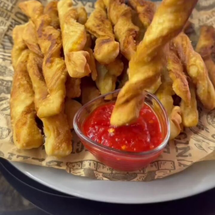 Golden spiral potato fries piled on a tray, one snapped in half showing a crisp, airy interior.