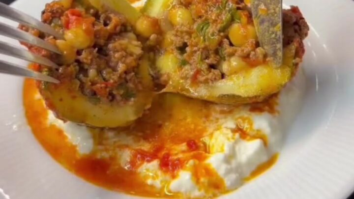 Stuffed round zucchini with beef and chickpeas in a rich tomato gravy, garnished with fresh herbs.